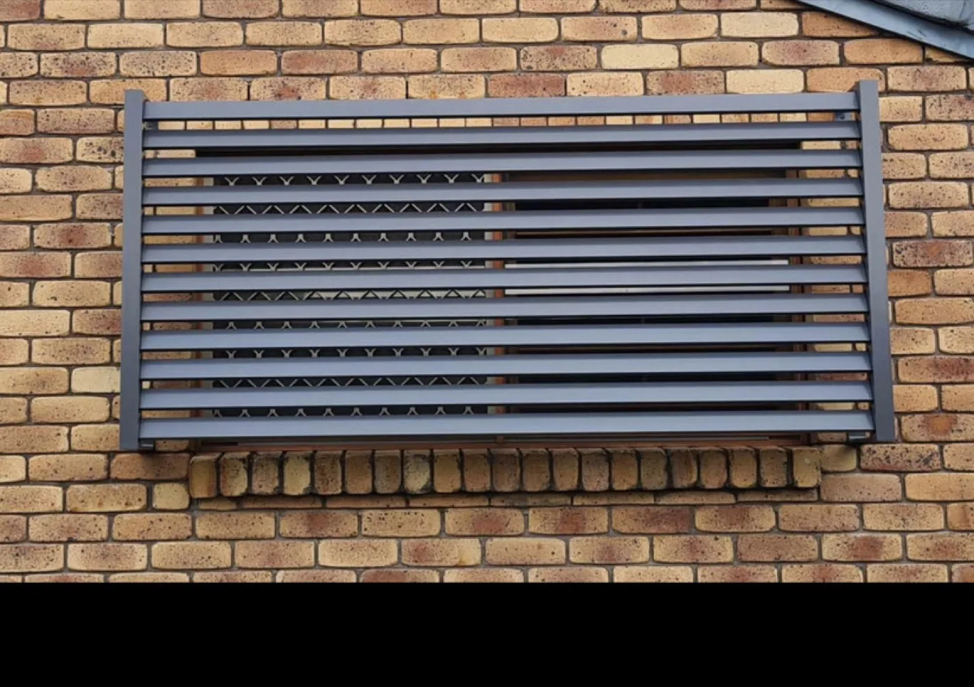 Grey aluminium louvre security screen over a window on cream brick