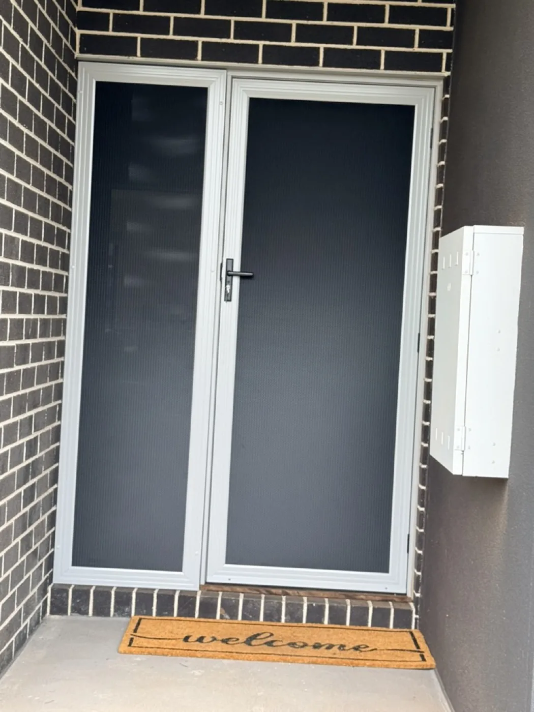 Silver French-style double security doors on a dark brick entrance