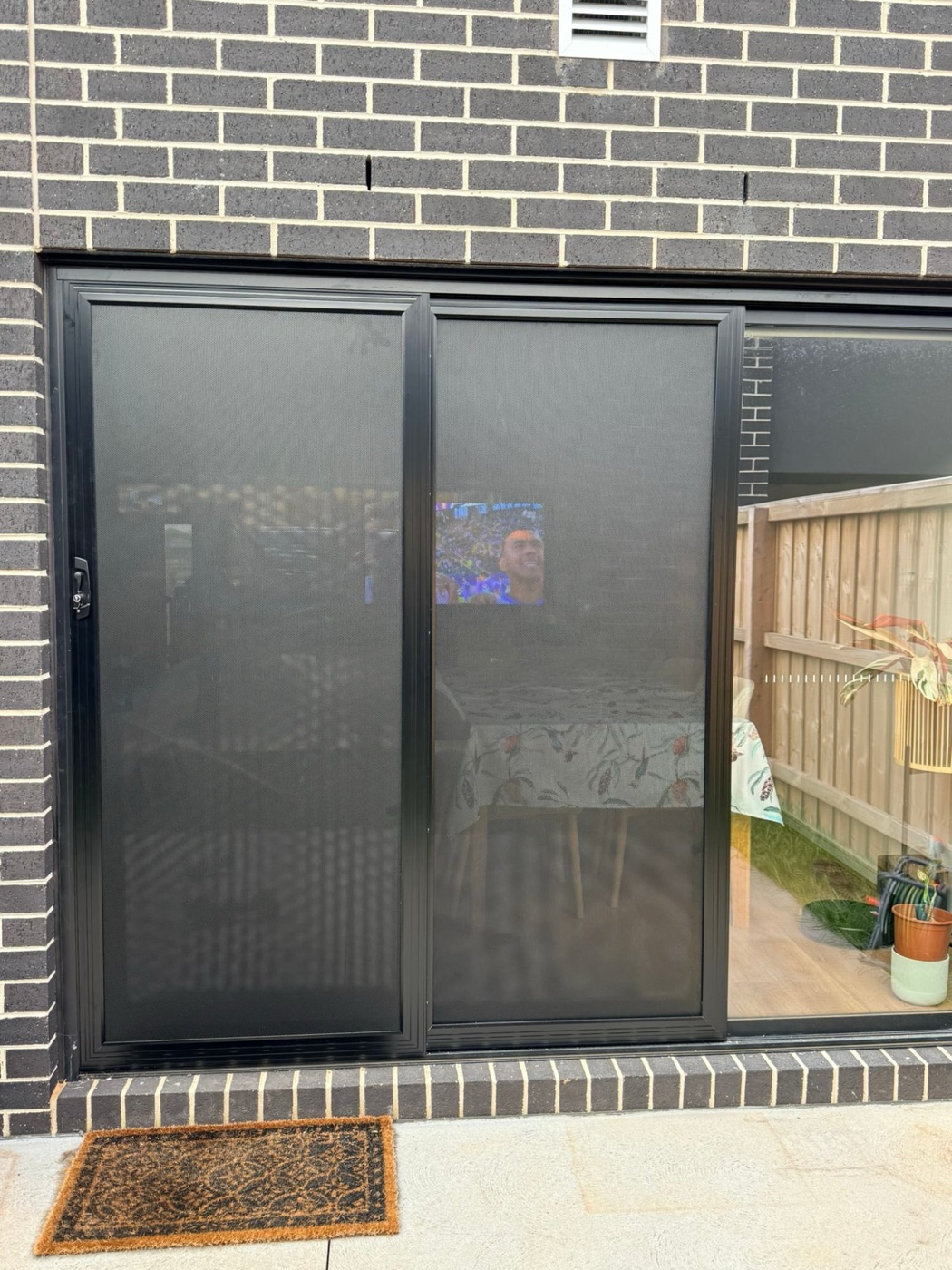 Black triple-track sliding security doors on a bluestone brick home