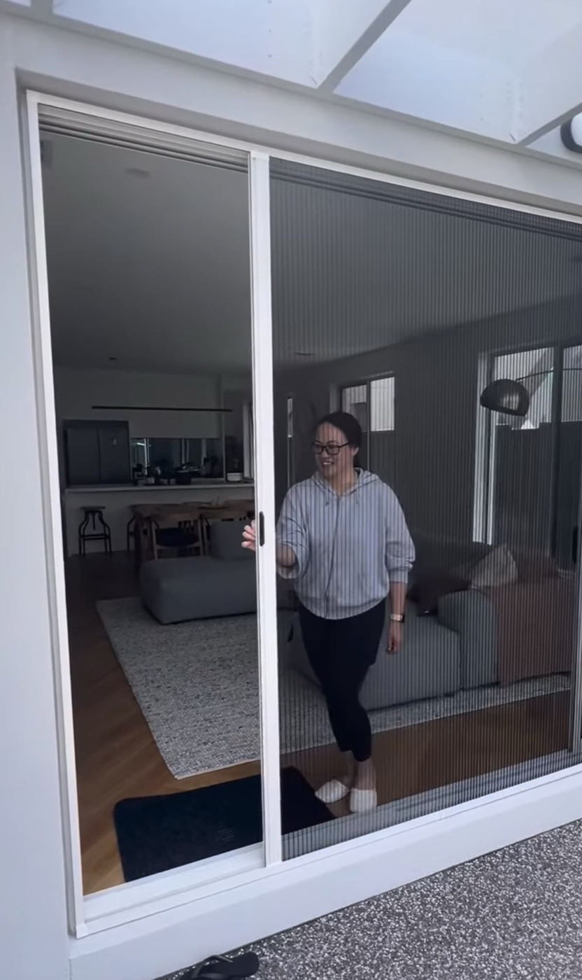 Happy customer gliding a pleated retractable fly screen across a wide sliding door opening
