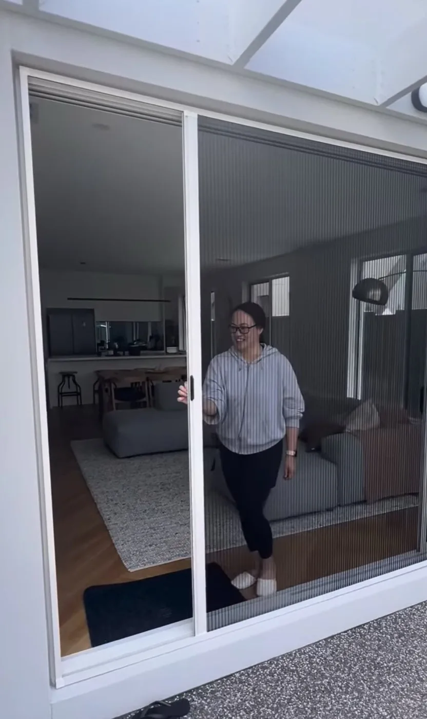 Happy customer gliding a pleated retractable fly screen across a wide sliding door opening
